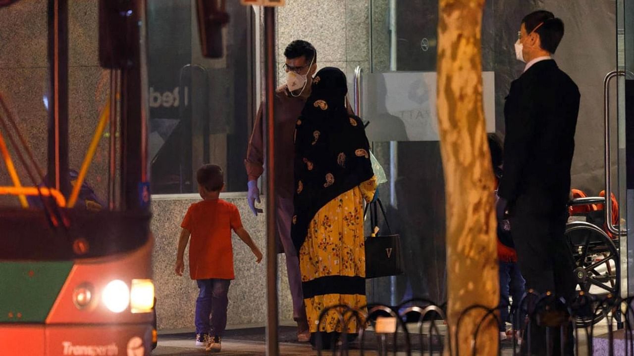 A family, part of more than 90 Australian citizens and Afghan nationals who were evacuated from Afghanistan, steps off a bus as she arrives at a hotel to begin quarantine in Perth, Australia. Credit: AFP Photo