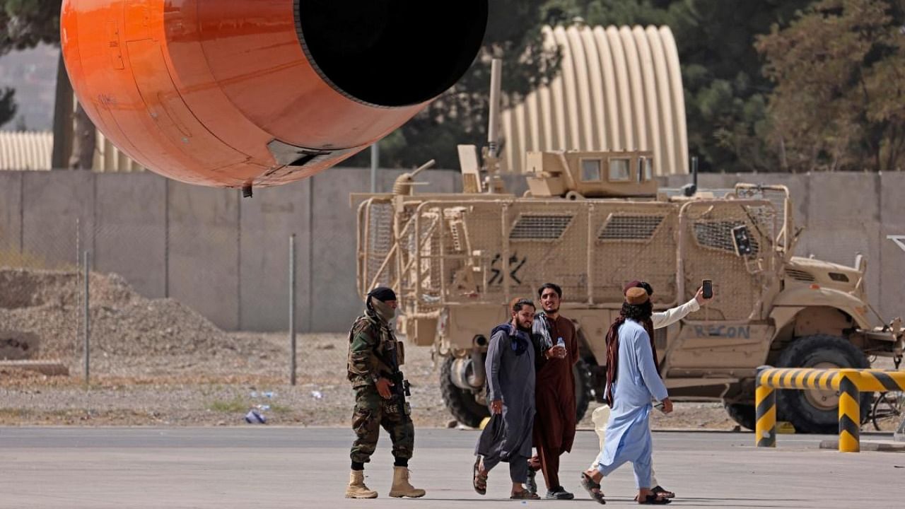 A Taliban fighter (L) walks near a parked armoured vehicle on the tarmac at the airport in Kabul. Credit: AFP Photo