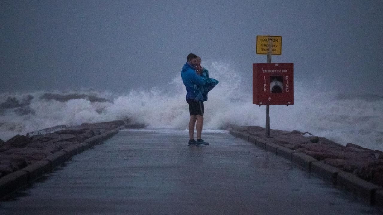 Local resident John Smith holds his 18-month-old son Owen as he stands near breaking waves on a pier ahead of the arrival of Tropical Storm Nicholas in Galveston, Texas, US, September 13, 2021. Credit: Reuters Photo
