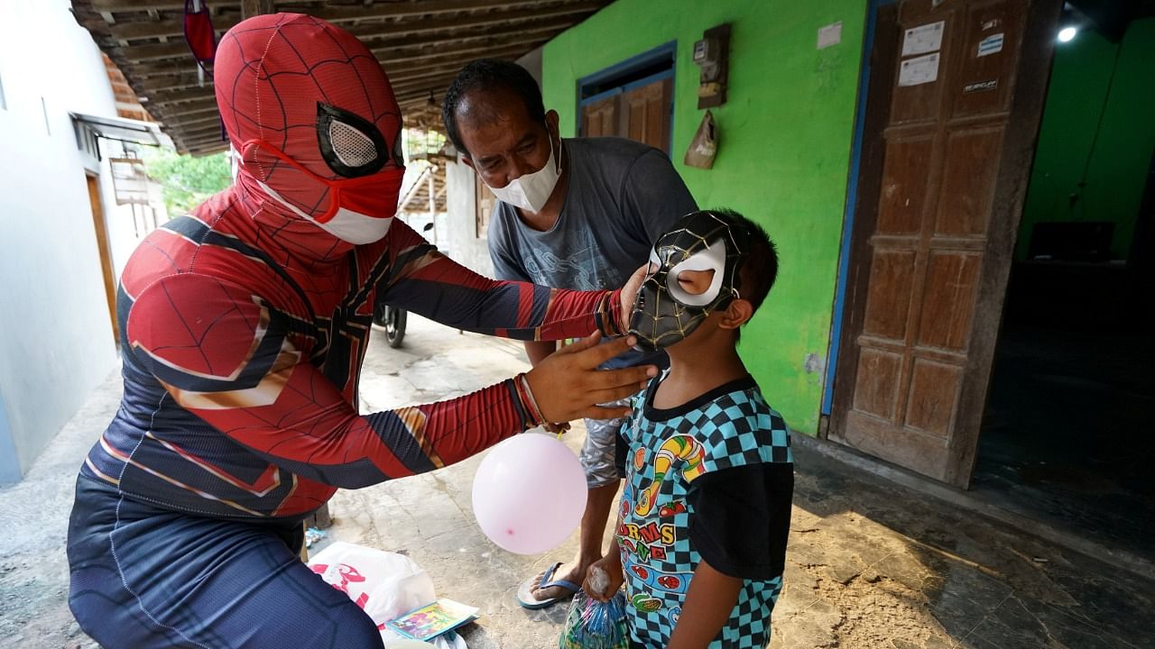 Agus Widanarko, 40, wears a superhero costume as he entertains a boy whose mother died from the coronavirus disease. Credit: Reuters Photo
