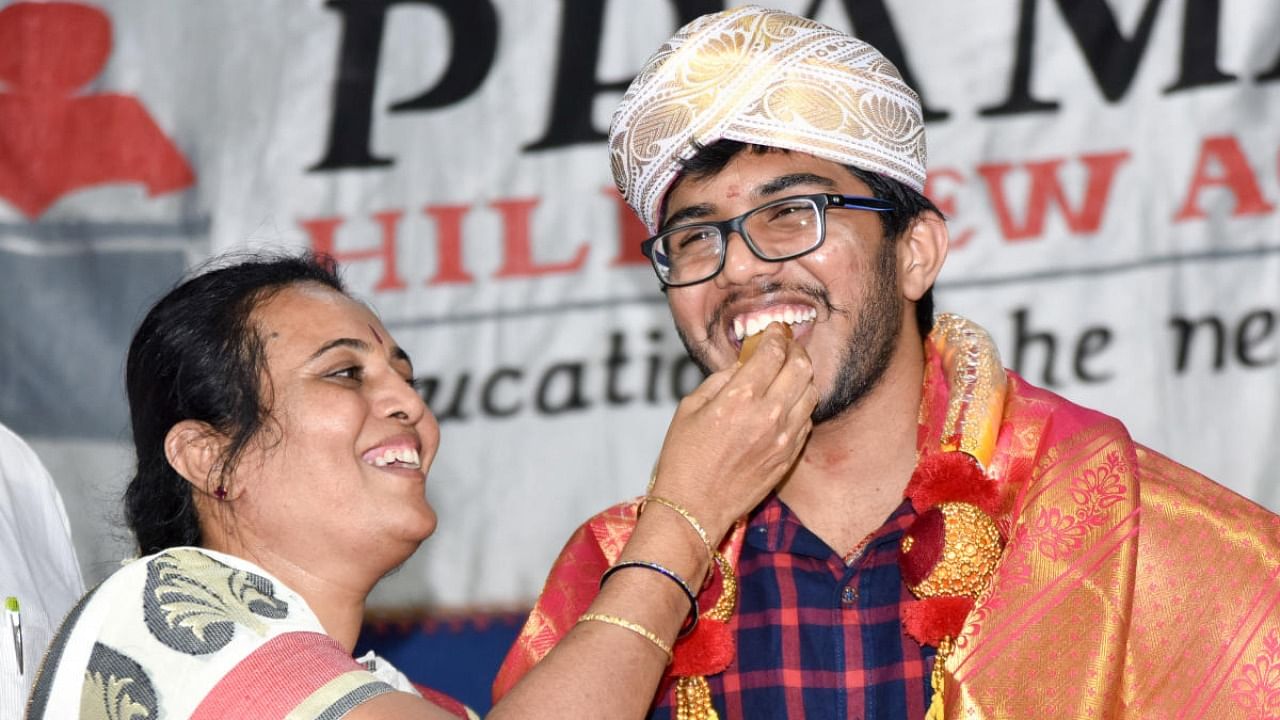 M S Leelavathy offers sweet to her son H K Meghan in Mysuru, on Monday. Credit: DH Photo