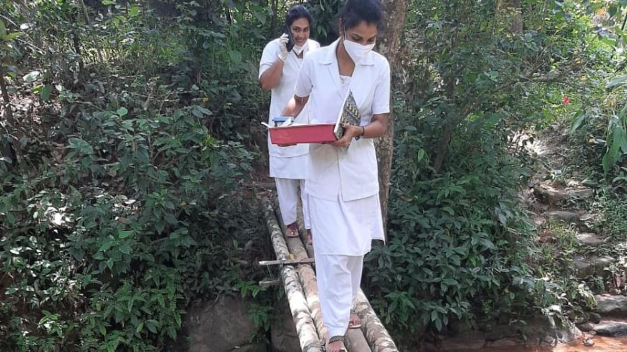 Health assistants crossing a delicate bridge to travel to a house to administer vaccines to a bed ridden person at Kaniyoor. Credit: DH photo