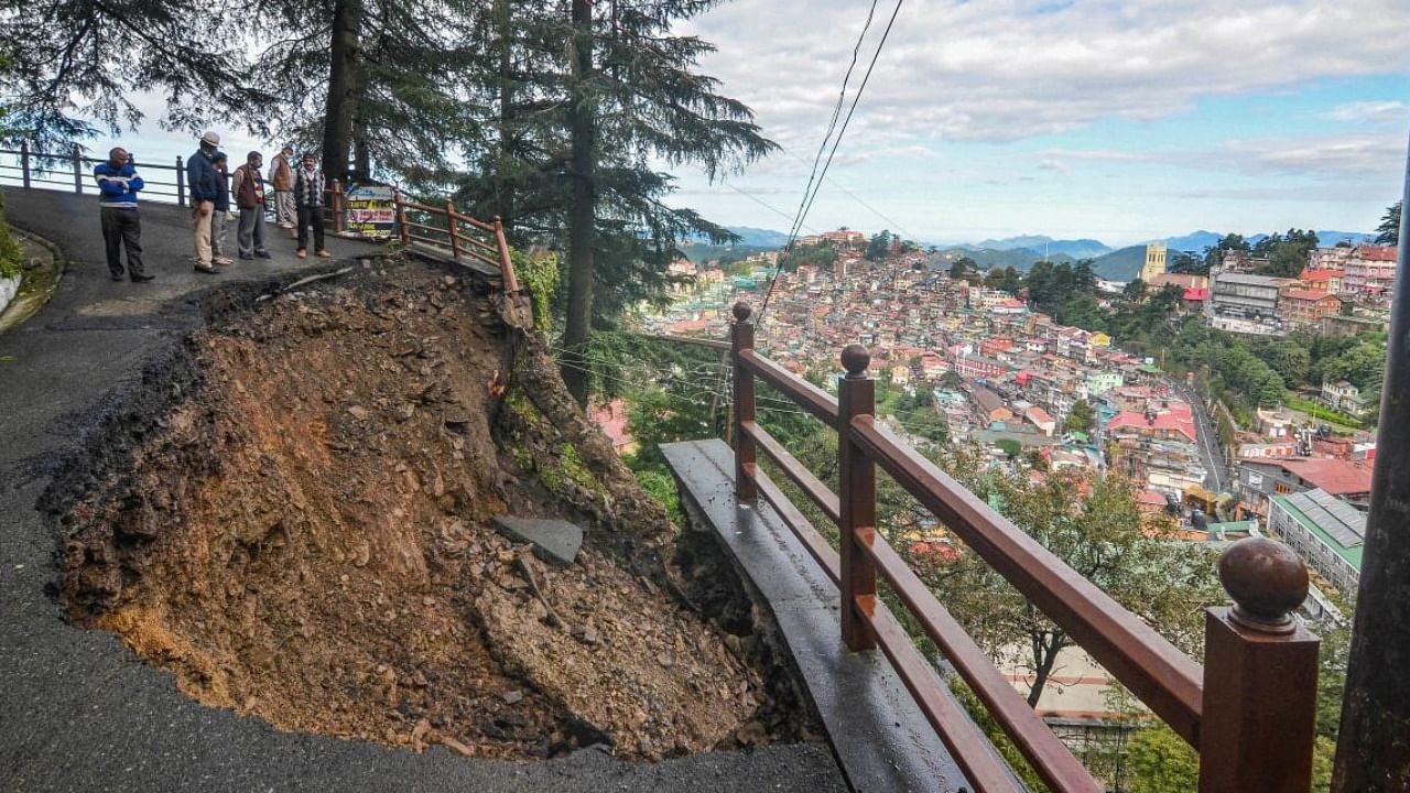Commuters stand near the caved-in portion of a road after heavy rainfall, in Shimla. Credit: PTI Photo