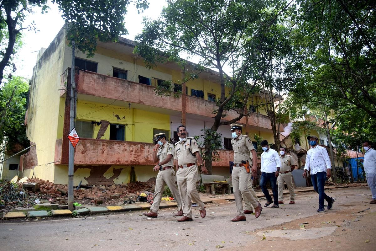 Policemen walk past the Bamul staff quarters inside the KMF campus near Dairy Circle, Bengaluru, on Tuesday. A portion of the building caved in due to the "loosening of the soil". Credit: DH Photo/Pushkar V