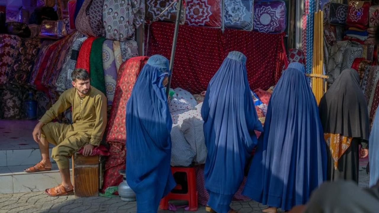 In this picture taken on September 22, 2021, women walk past a stall in a market area in Kabul. Credit: AFP Photo