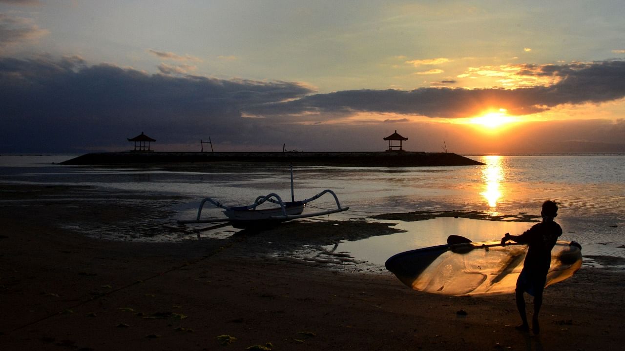 A man carries a canoe during sunrise at a beach in Sanur on Indonesia's resort island of Bali on September 28, 2021. Credit: AFP Photo