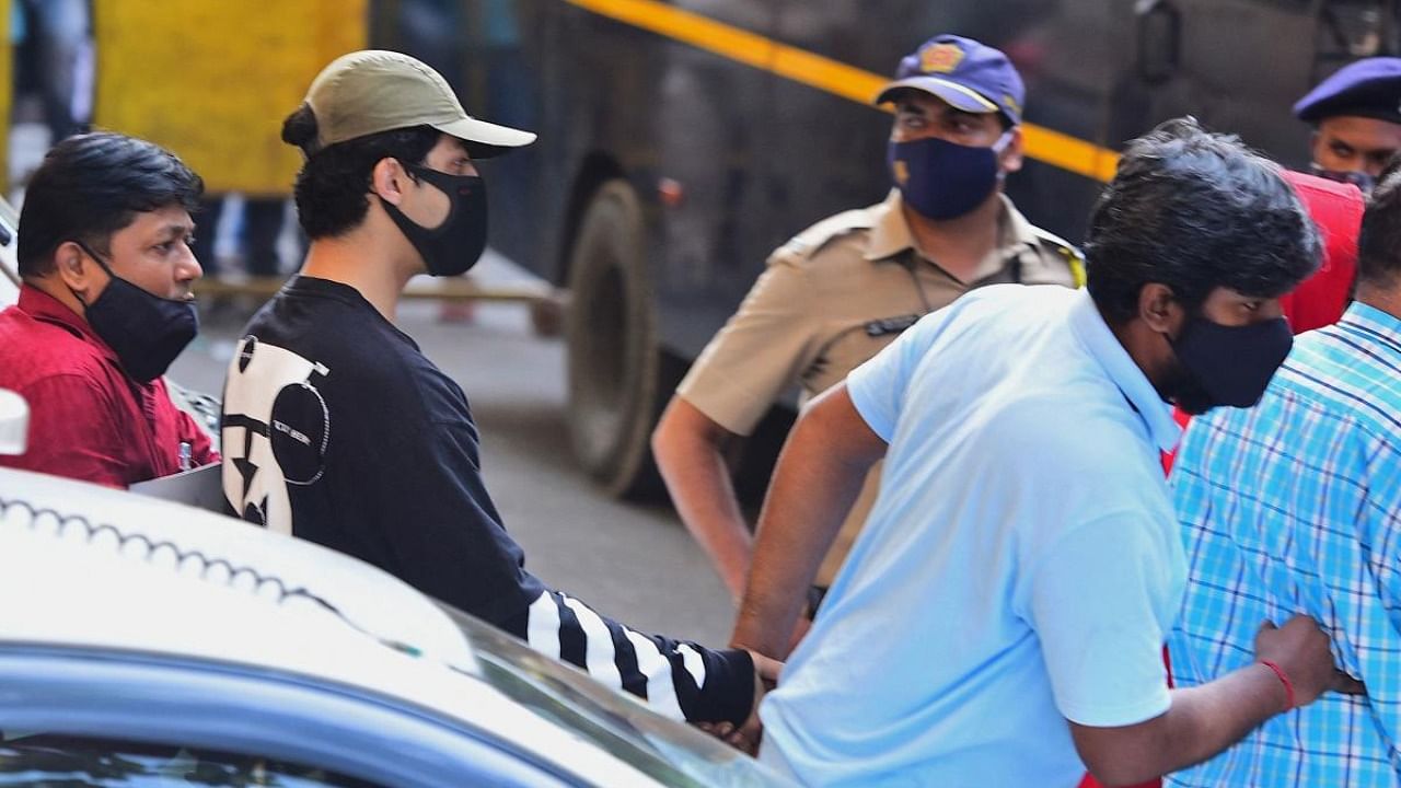 Bollywood actor Shah Rukh Khan's son Aryan Khan (2L) is being escorted by law enforcement officials outside the Narcotics Control Bureau (NCB) office after he was allegedly brought in for questioning along with others following a raid at a party on a cruise ship, in Mumbai. Credit: AFP Photo