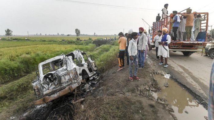 People take a look at the overturned SUV which was destroyed in the violence during farmers' protest at Tikonia area of Lakhimpur Kheri district. Credit: PTI Photo
