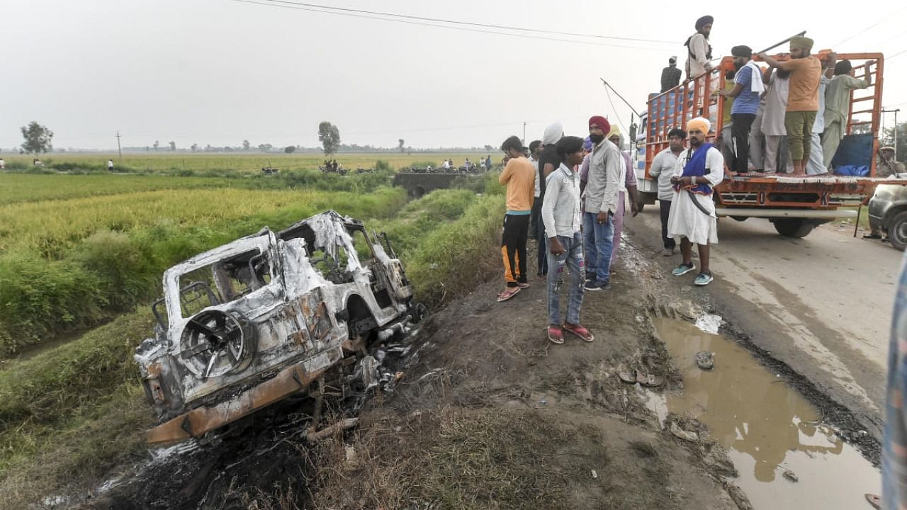 People take a look at the overturned SUV which destroyed in the violence during farmers' protest, at Tikonia area of Lakhimpur Kheri district. Credit: PTI Photo