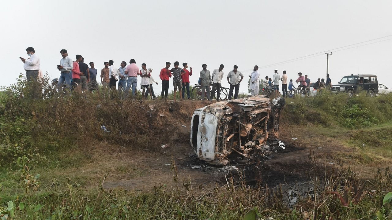 People take a look at the overturned SUV which was destroyed in violence during farmers' protest, at Tikonia area of Lakhimpur Kheri district, Monday. Credit: PTI File Photo