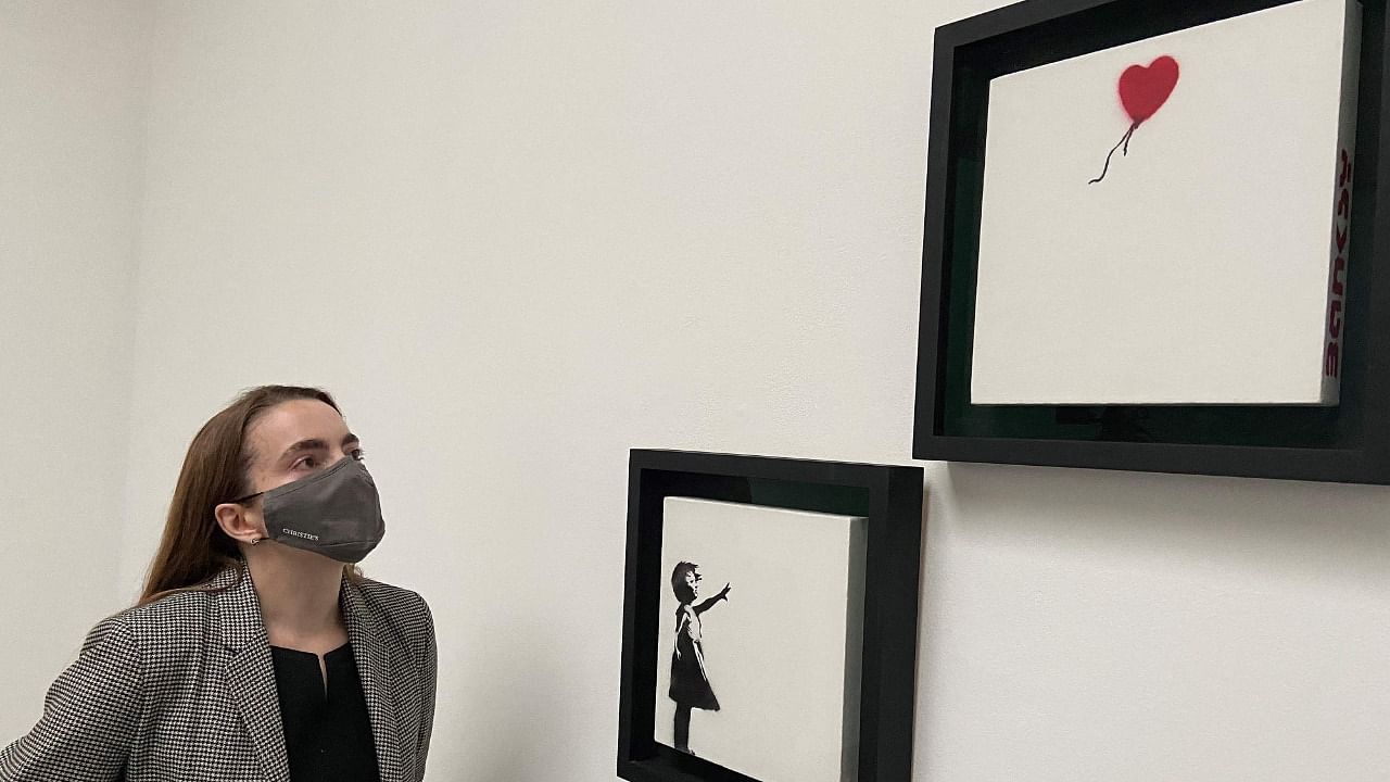 A gallery employee poses with an artwork entitled 'Girl and Balloon' (Diptych) by Banksy, during a photocall at Christie's auction house in central London on October 1, 2021. Credit: AFP Photo