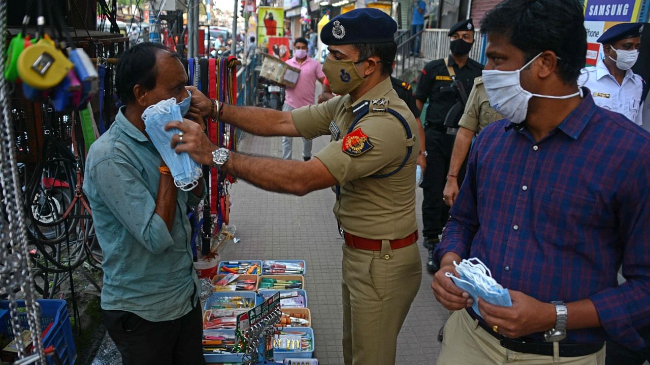 Siliguri metropolitan police commissioner Gaurav Sharma (C) distributes a facemask to a vendor as Darjeeling's district magistrate S Ponnambalam (R) watches during an awareness campaign against the Covid-19 coronavirus at a market ahead of the Durga Puja festival in Siliguri on October 10, 2021. Credit: AFP Photo