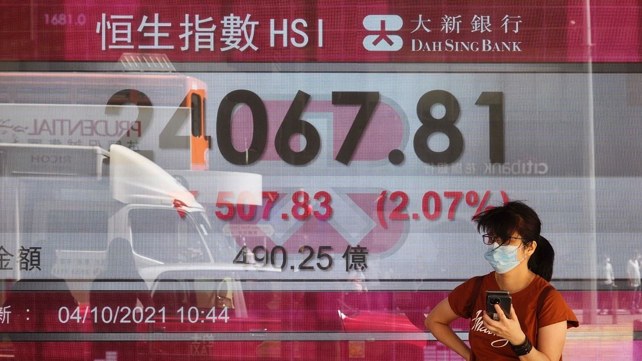 A woman walks past a bank's electronic board showing the Hong Kong share index at Hong Kong Stock Exchange. Credit: AP/PTI File Photo