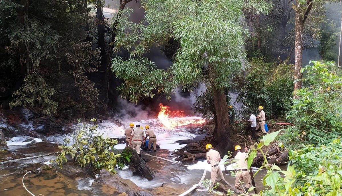 Firemen try to douse the blaze in a stream following a tanker accident at Aarathibail Ghat on NH-63 near Yellapur in Uttara Kannada district on Wednesday. Credit: DH Photo