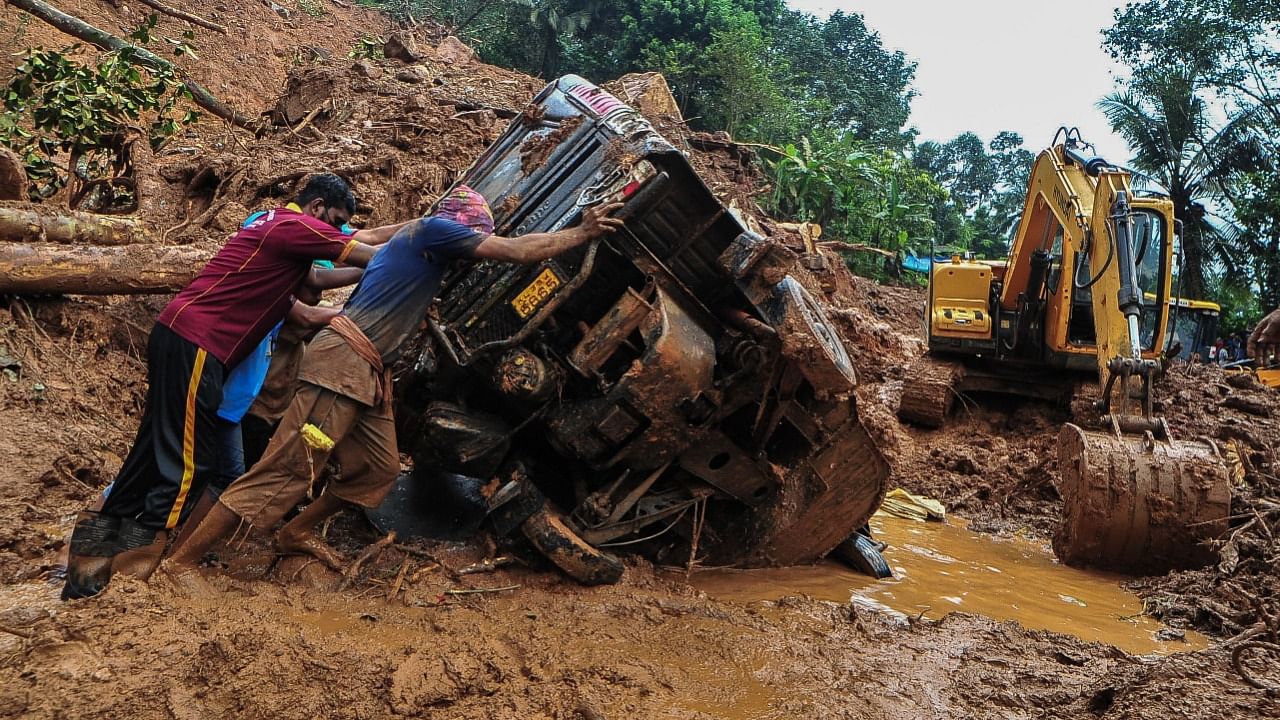 Rescue workers push a overturned vehicle stuck in the mud and debris at a site of a landslide claimed to be caused by heavy rains in Kokkayar in Kerala. Credit: AFP Photo