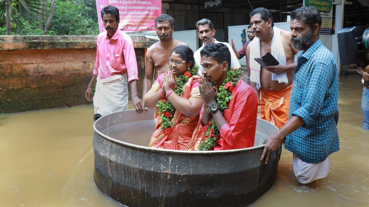 Couple Akash and Aishwarya wade through a waterlogged area in a large cooking vessel before their marriage, in Alappuzha. Credit: PTI Photo