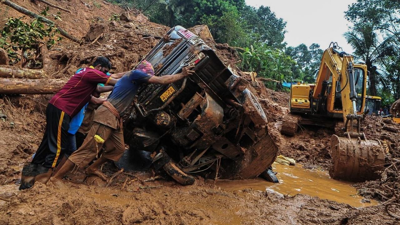 Rescue workers push a overturned vehicle stuck in the mud and debris at a site of a landslide claimed to be caused by heavy rains in Kokkayar in Kerala. Credit: AFP Photo