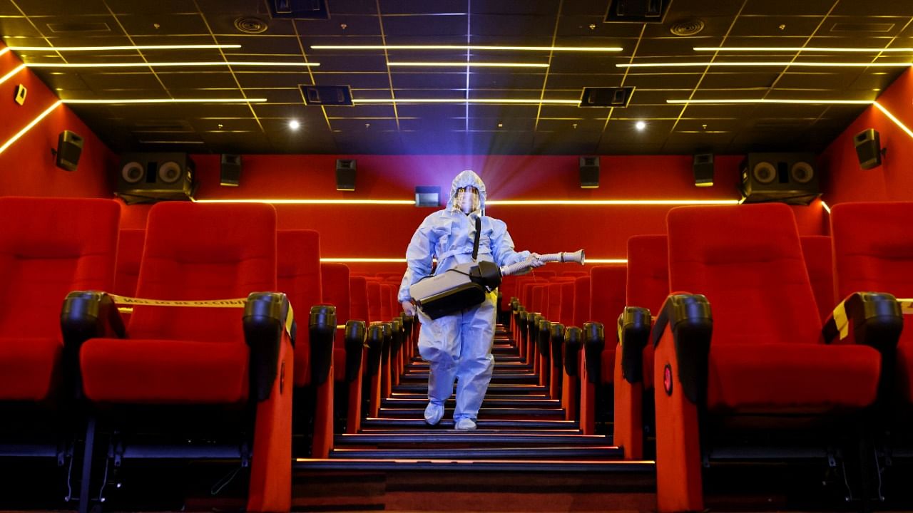 A worker wearing personal protective equipment sanitizes seats inside a movie theatre ahead of its reopening, in Mumbai. Credit: Reuters File Photo