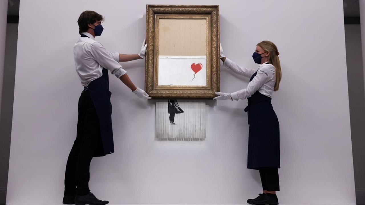 A gallery assistant poses by 'Love is in the Bin', an artwork by Banksy, which will be for sale in an auction, at Sotheby's in London, Britain. Credit: Reuters Photo