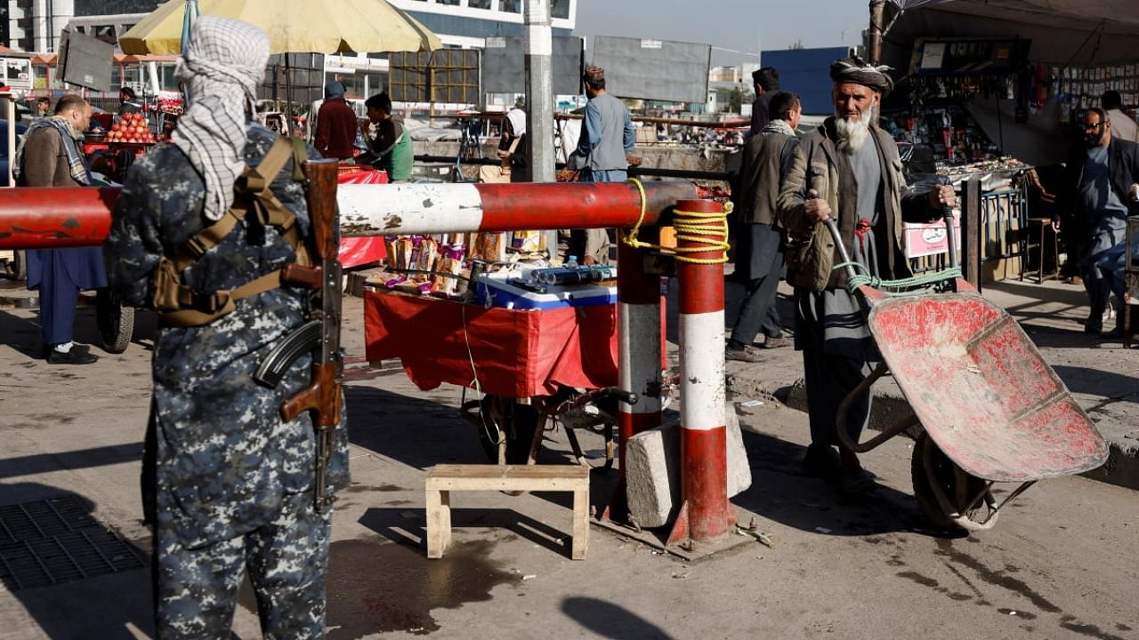 A man pushes a wheelbarrow as a Taliban fighter stands guard at the market in Kabul. Credit: Reuters photo