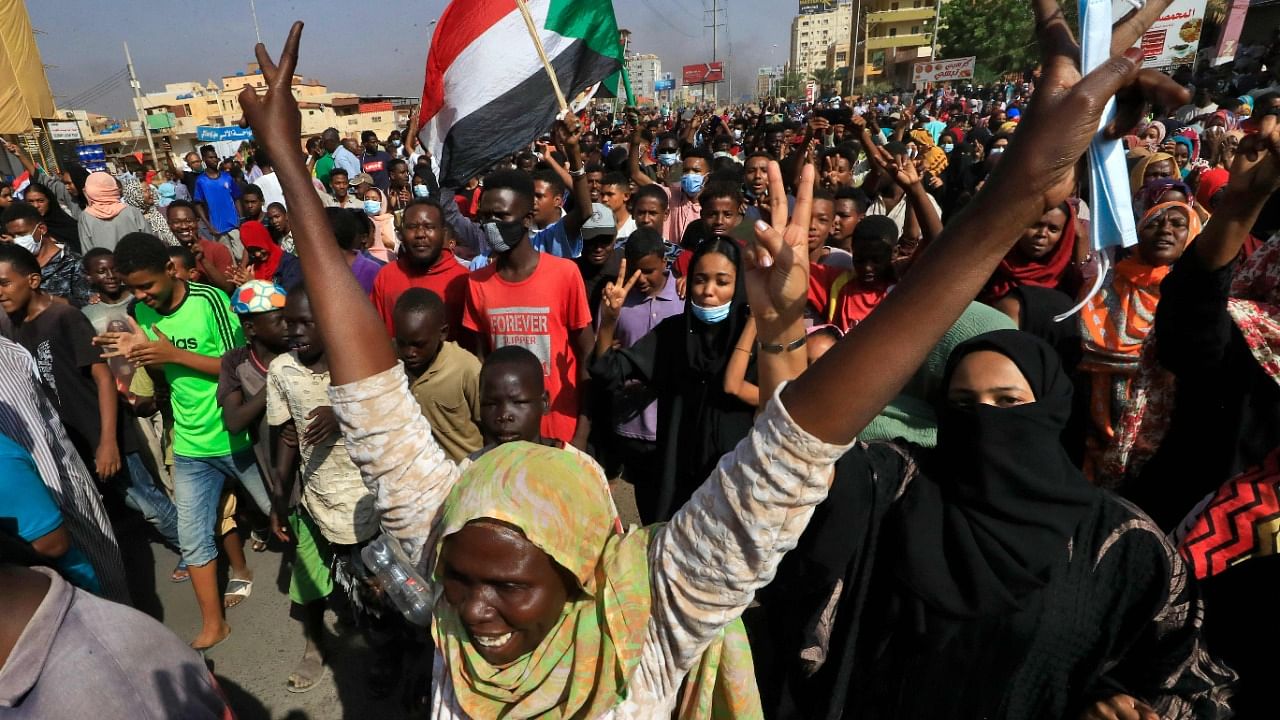 Sudanese protesters lift national flags as they rally on 60th Street in the capital Khartoum, to denounce overnight detentions by the army of government members. Credit: AFP Photo