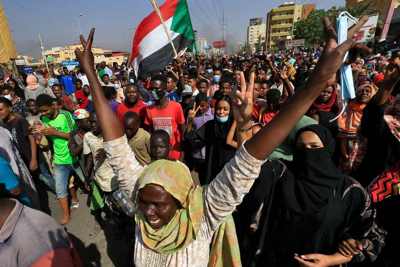 Sudanese protesters lift national flags as they rally on 60th Street in the capital Khartoum, to denounce overnight detentions by the army of government members. Credit: AFP Photo