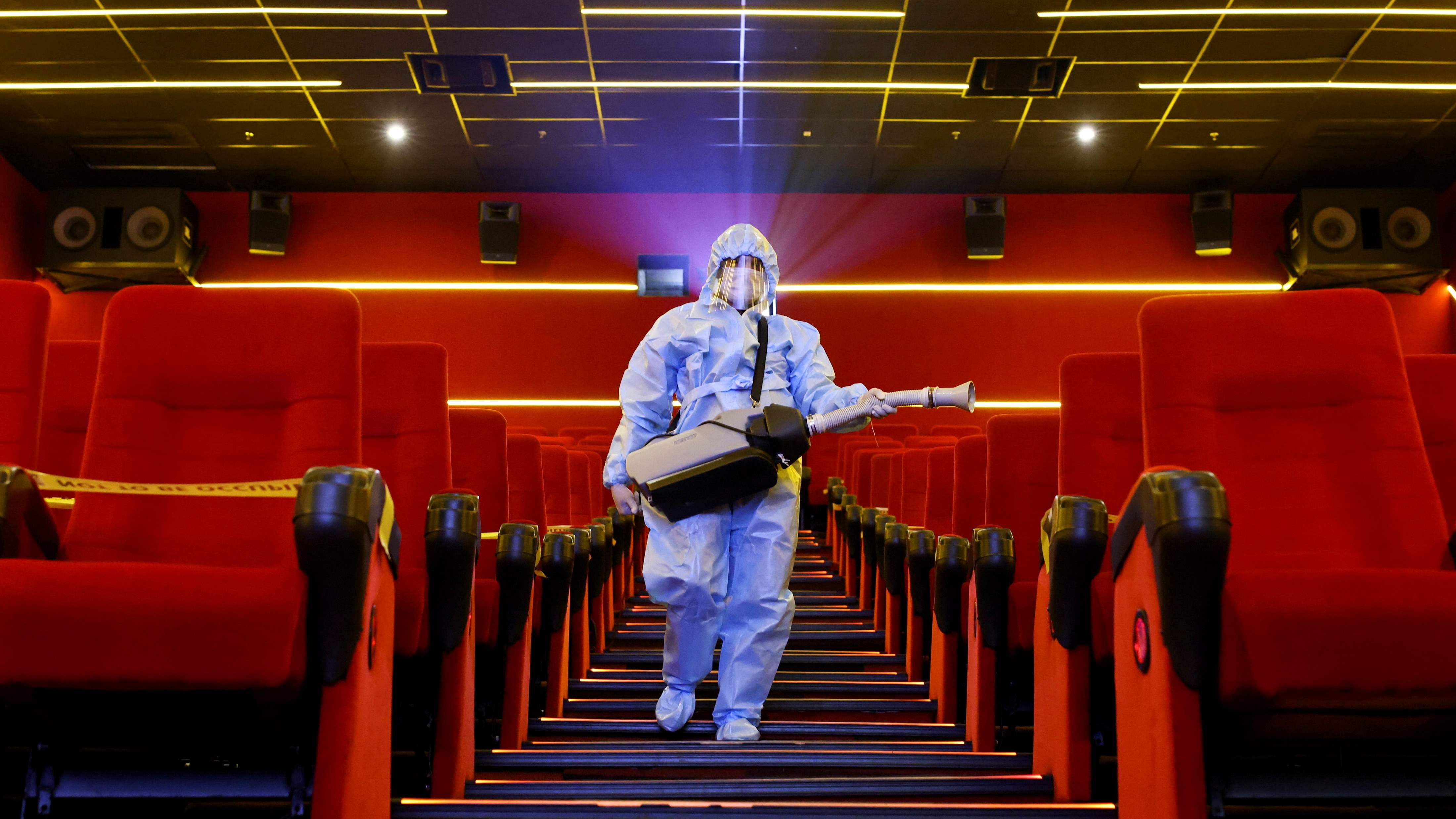 A worker wearing personal protective equipment (PPE) sanitizes seats inside a movie theatre. Credit: Reuters File Photo