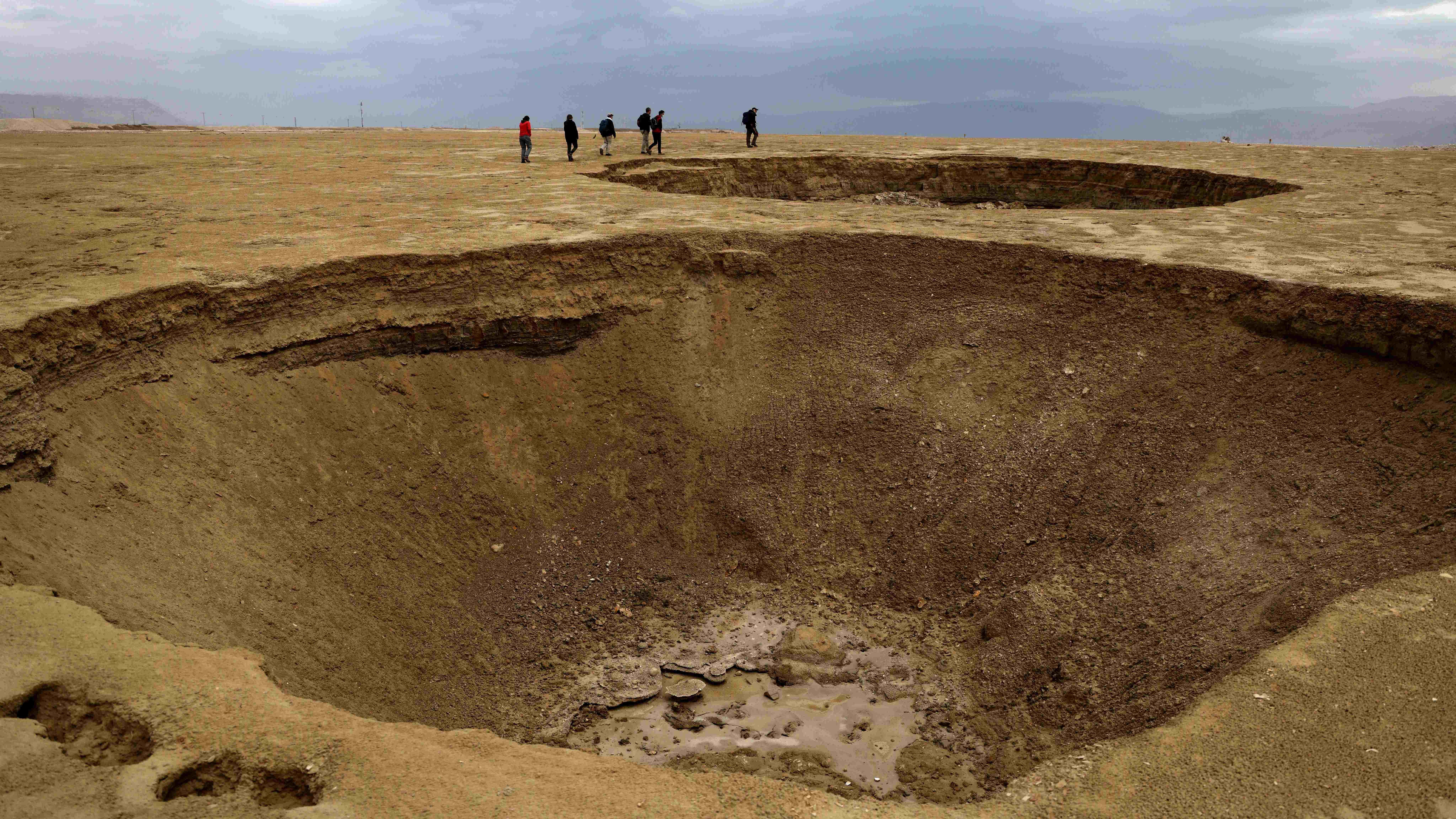 Hikers walk next to sinkholes across a dried-up sea area which exposed and created a salt plain, some 20 Km south of the Israeli Kibbutz Ein Gedi in the southern part of the Dead Sea. Credit: AFP Photo