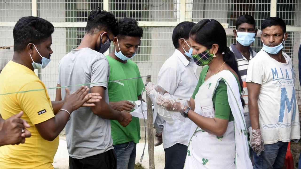 A health worker distributes disposable gloves to voter before casting vote during by-polls election at Mariani constituency in Jorhat. Credit: PTI photo