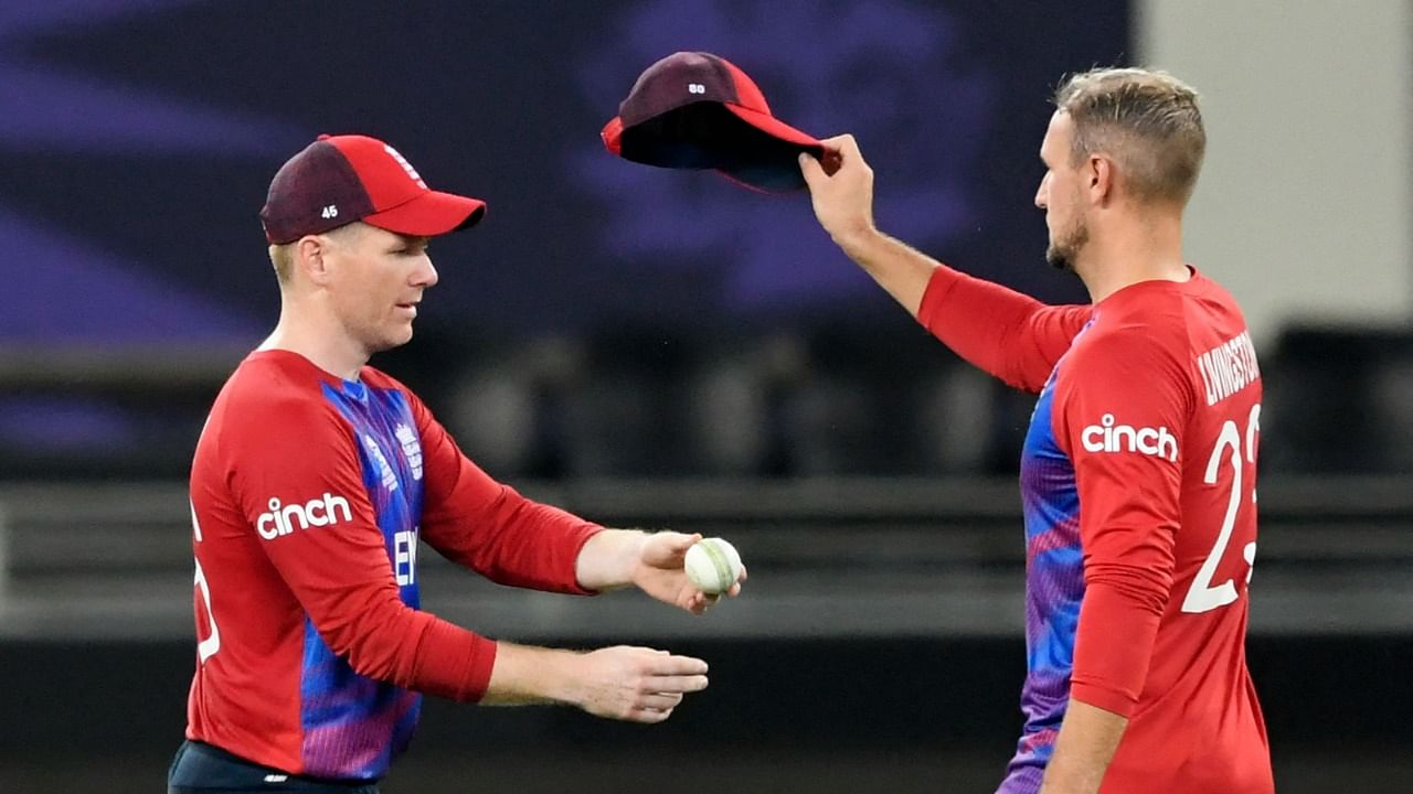 England's captain Eoin Morgan (L) gives the ball to his teammate Liam Livingstone during the ICC men’s Twenty20 World Cup cricket match between Australia and England at the Dubai International Cricket Stadium in Dubai on October 30, 2021. Credit: AFP Photo