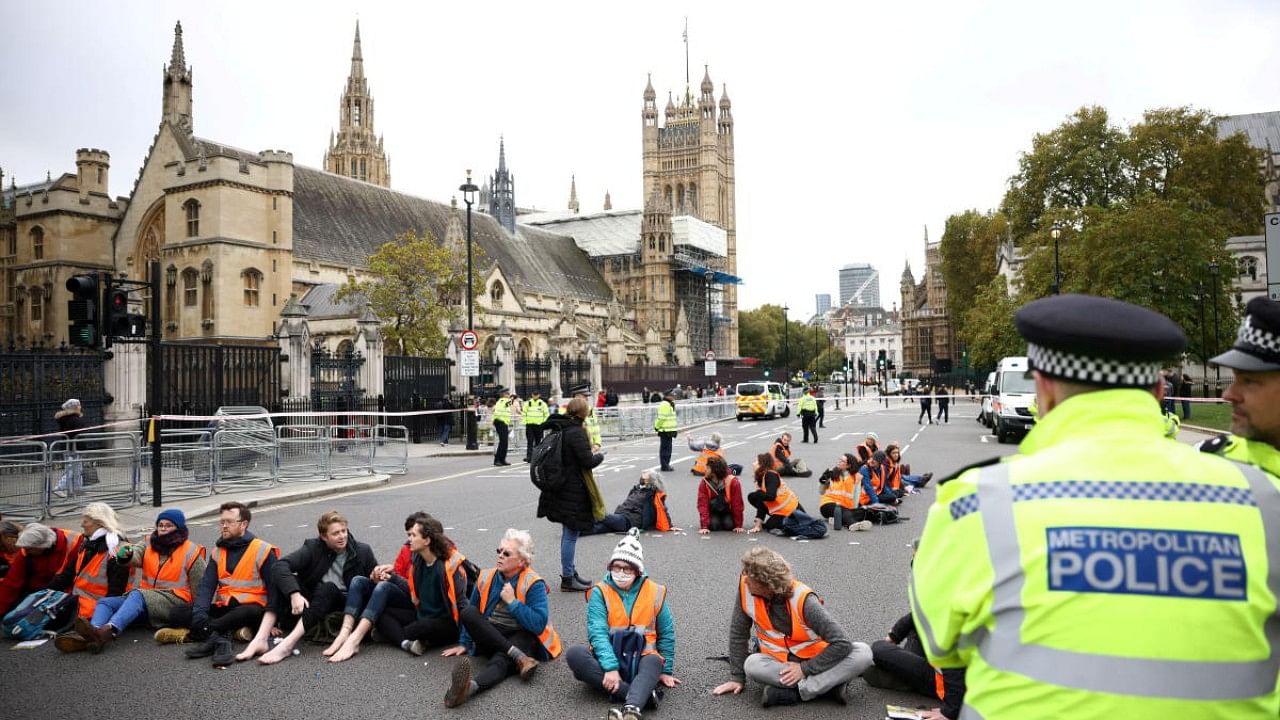 Insulate Britain activists have their hands and feet glued to the road as they block a road outside the Houses of Parliament during a protest in London. Credit: Reuters Photo