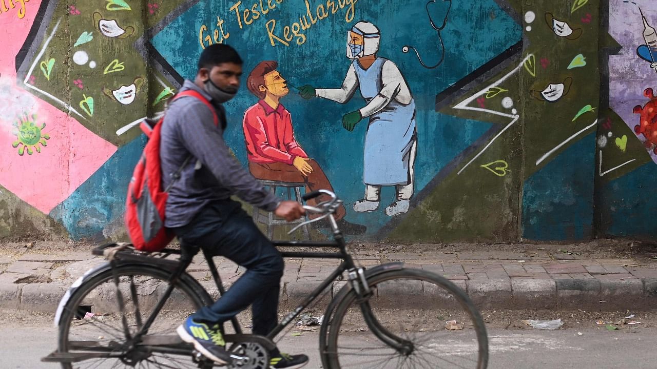 A cyclist rides past a mural depicting a health worker conducting Covid-19 coronavirus testing in New Delhi on November 6, 2021. Credit: AFP Photo