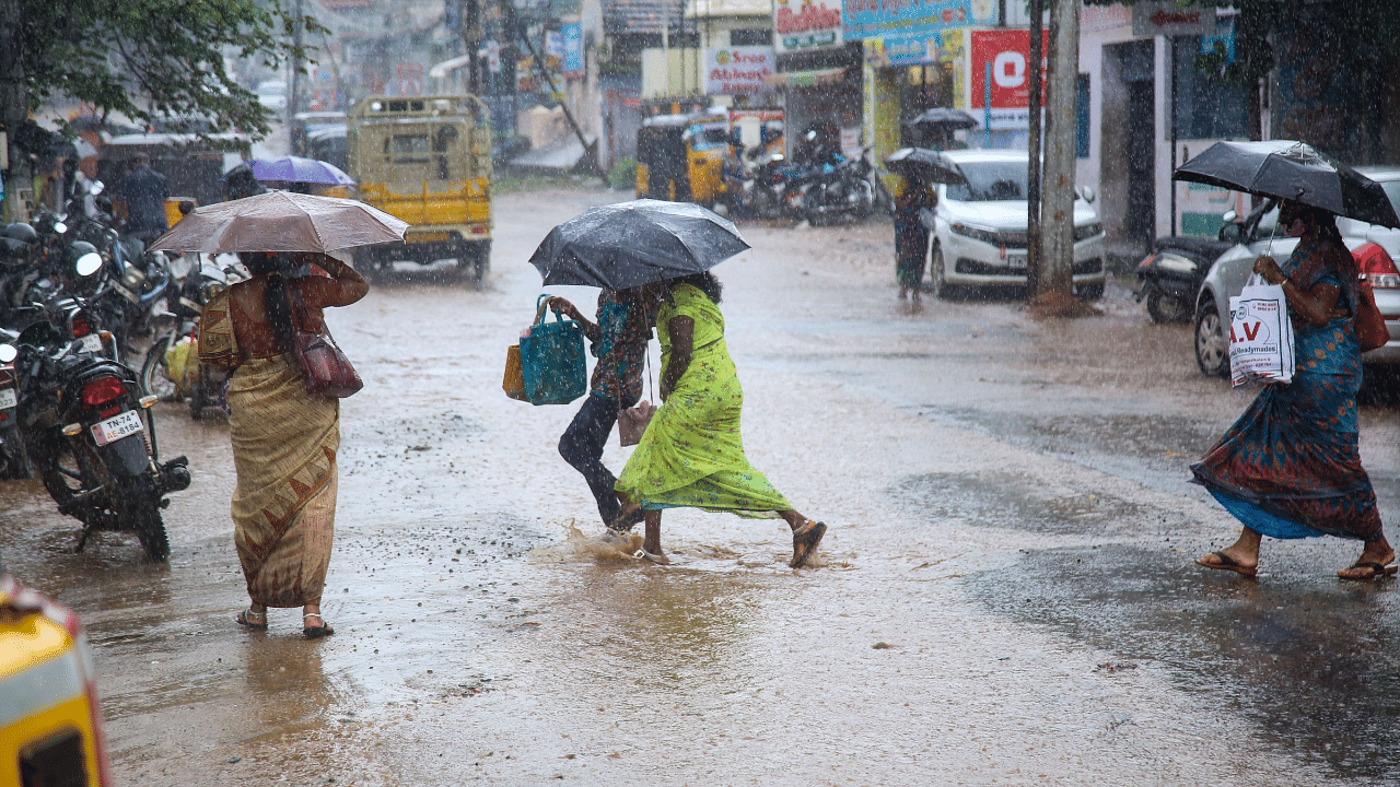 Commuters cross a road during heavy rainfall in Kanyakumari. Credit: PTI Photo