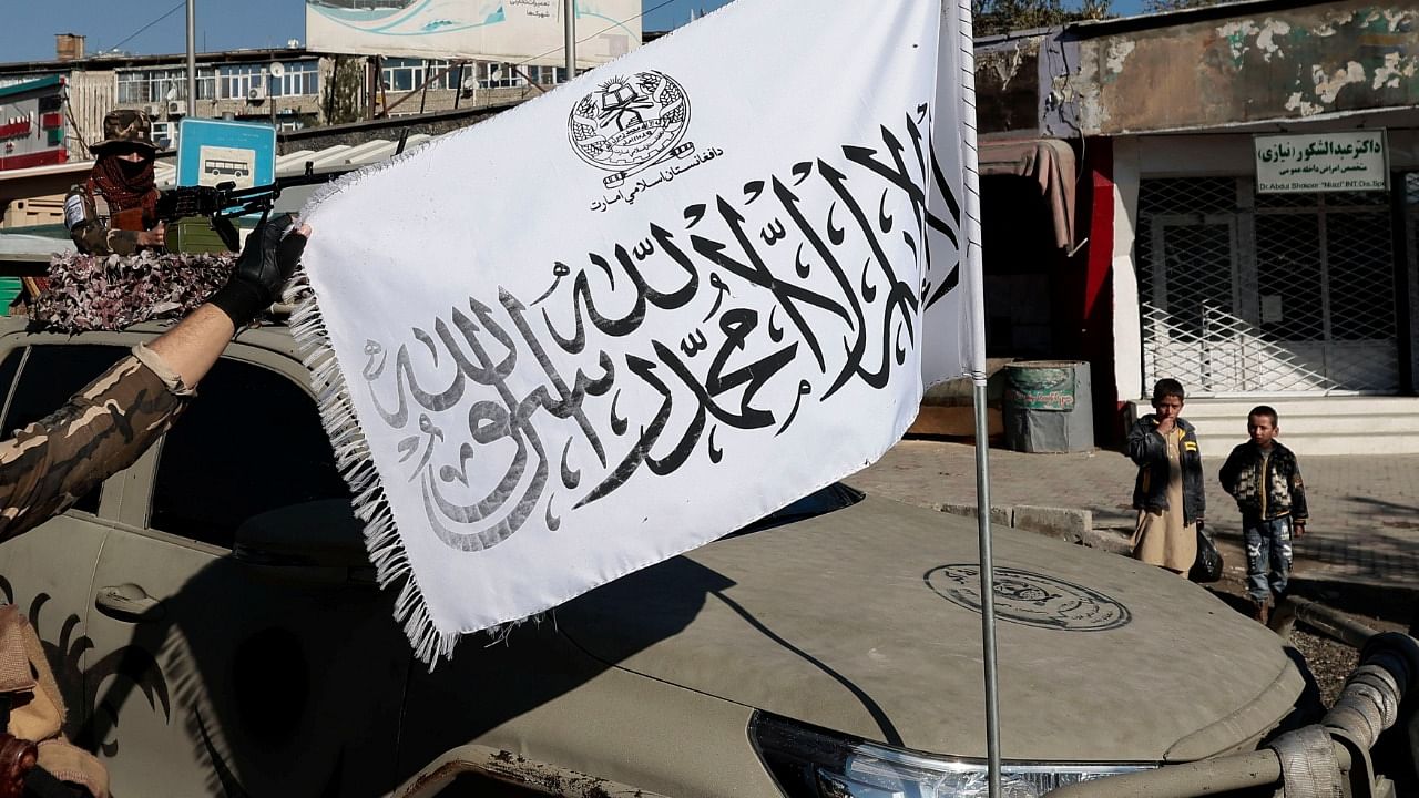 A Taliban fighter displays their flag as his comrade watches, at a checkpoint in Kabul, Afghanistan. Credit: Reuters File Photo