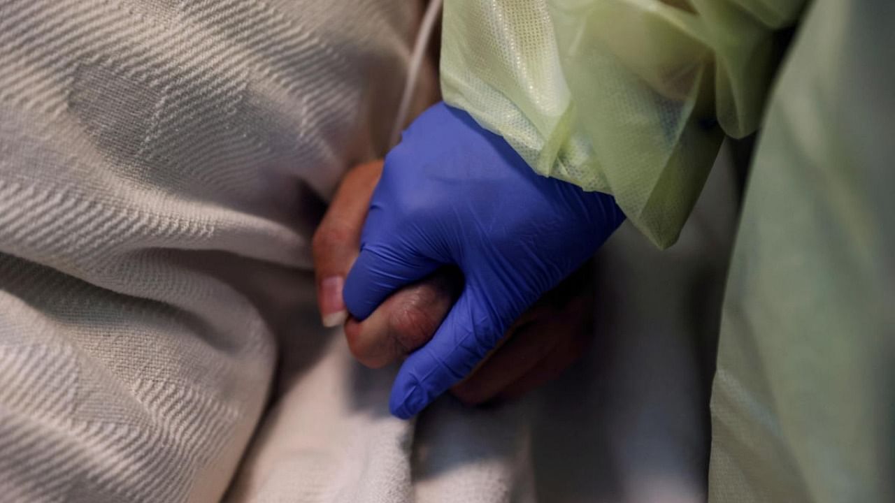 A woman in her personal protective equipment (PPE) gear holds the hand of a coronavirus disease (Covid-19) positive patient, in her isolation room at Madison Memorial Hospital in Rexburg, Idaho, US. Credit: Reuters Photo