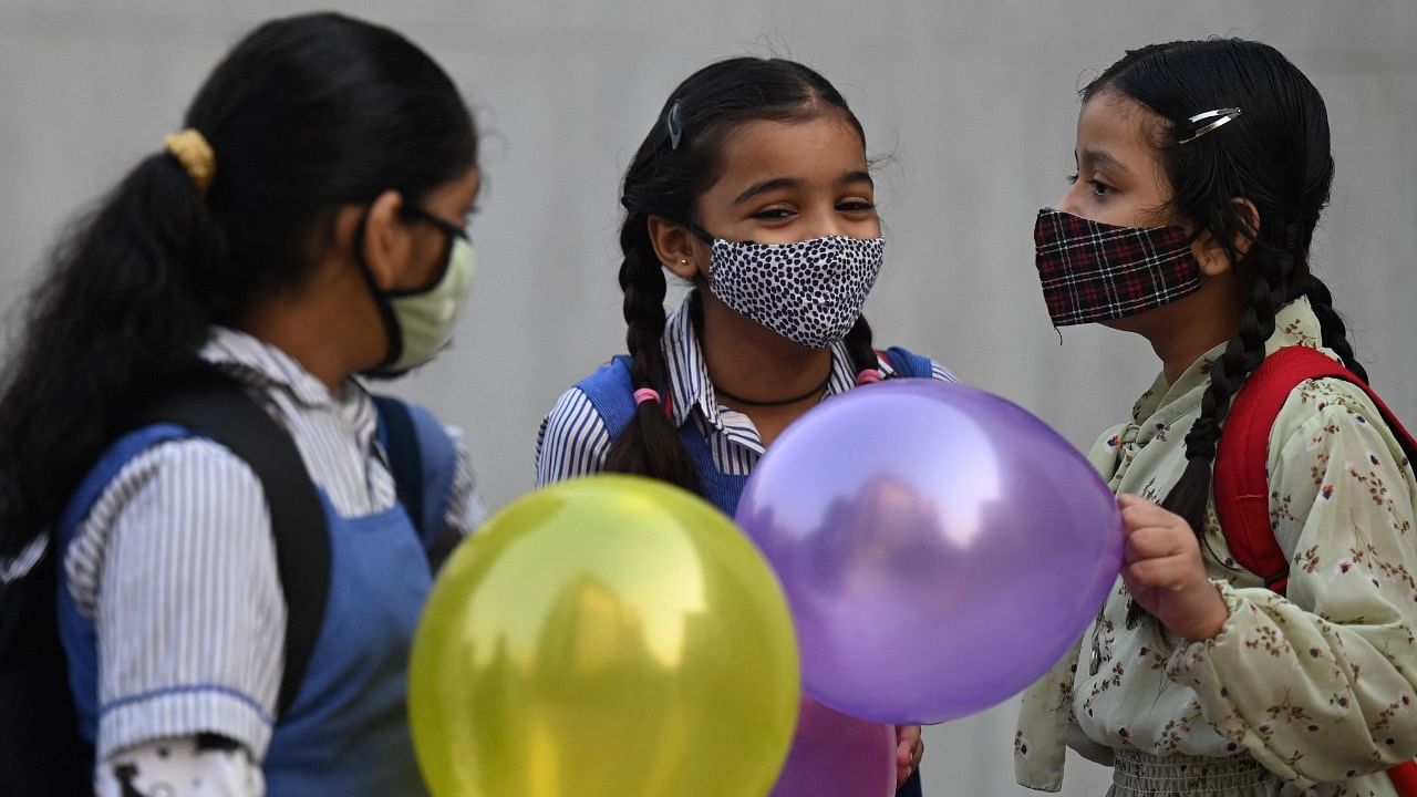 Children hold balloons as they enter their school in New Delhi on November 1, 2021 as schools reopen after months due to the Covid-19 coronavirus pandemic. Credit: AFP File Photo