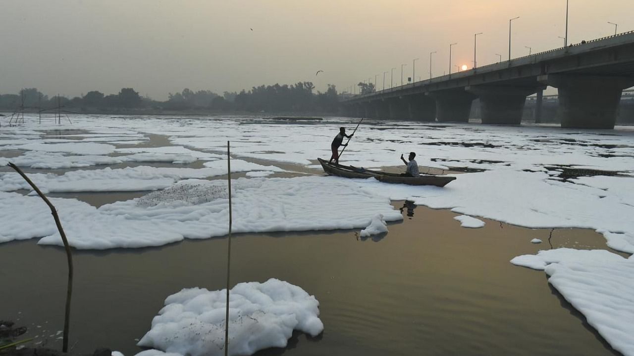 A boatman moves through a froth laden polluted Yamuna river, as smog engulfs the sky during sunset, at Kalindi Kunj in New Delhi. Credit: PTI Photo