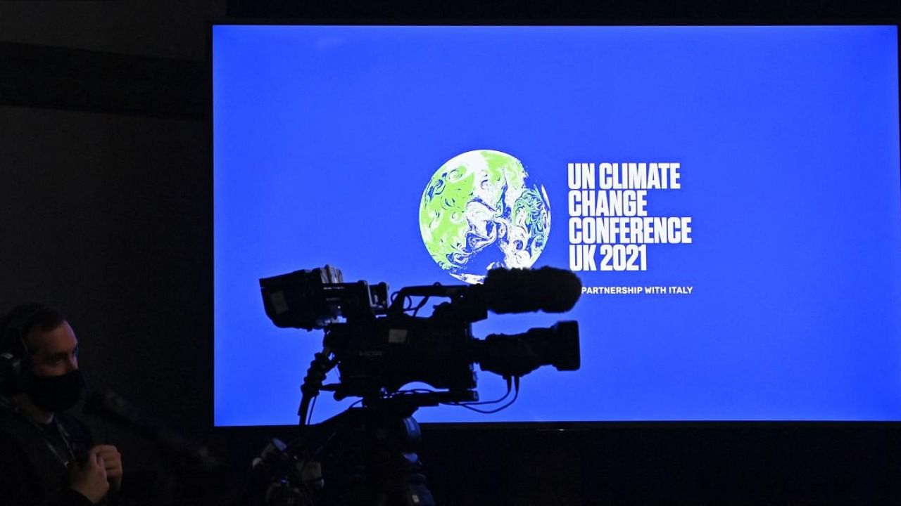 A television camera operator works in front of a COP26 logo displayed on a screen ahead of an event on the sidelines of the COP26 UN Climate Change Conference in Glasgow. Credit: AFP Photo