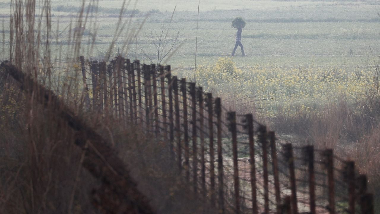 A farmer carries a sack of grass as he walks near the fenced border between India-Pakistan in Ranbir Singh Pura sector near Jammu. Credit: Reuters File Photo