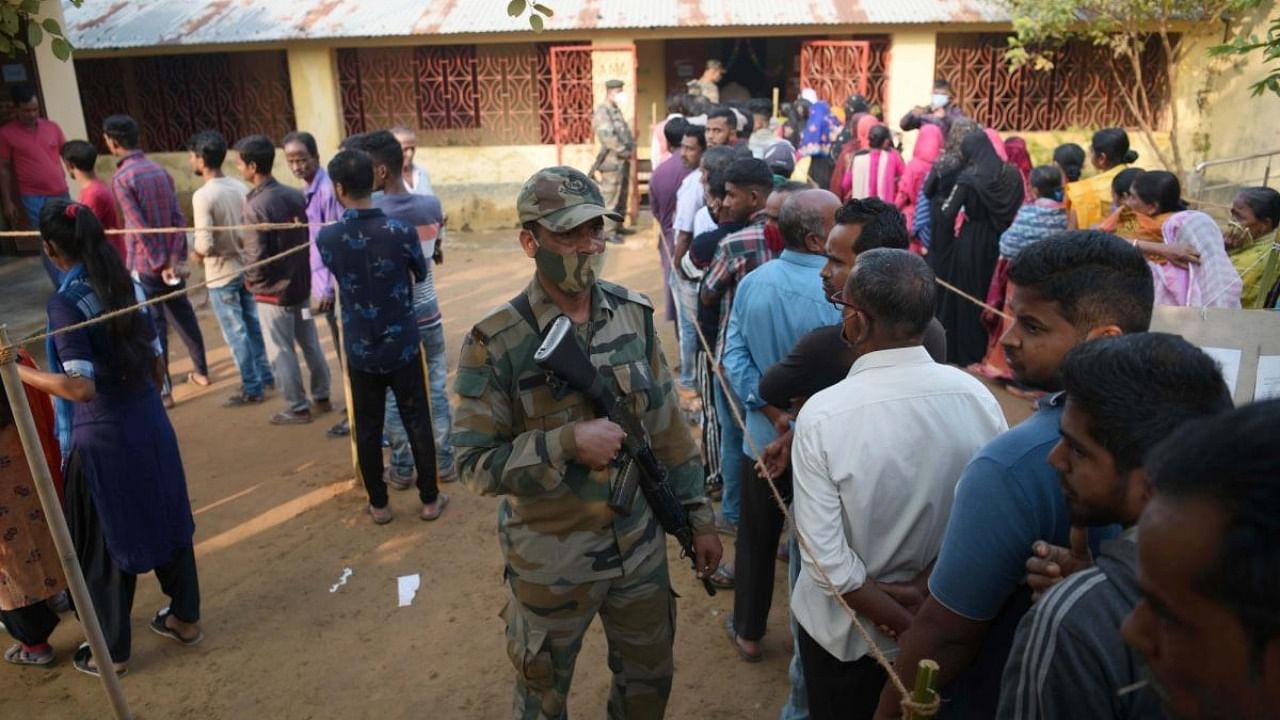 Armed security personnels stand guard as voters stand in que to cast their votes at a polling station during the Tripura Municipal Corporation election in Agartala. Credit: IANS Photo