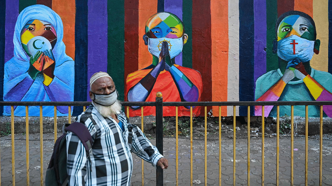 A man walks past a wall mural depiciting (L-R) a Muslim woman, a Buddhist monk and a Christian man all wearing masks to spread awareness about the Covid-19 coronavirus. Credit: AFP Photo