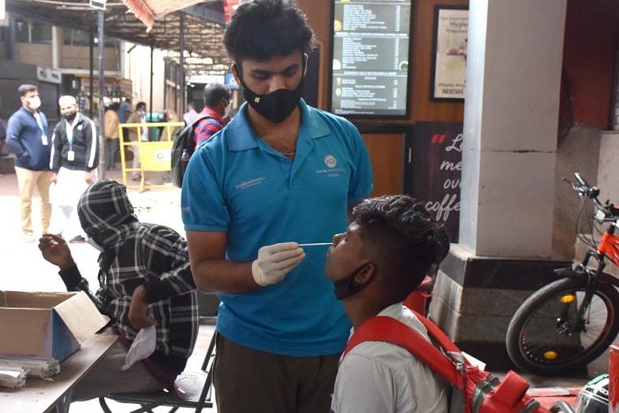 Health department volunteers collect swab samples for Covid testing at the KSR railway station on Saturday. Credit: DH Photo/B K Janardhan