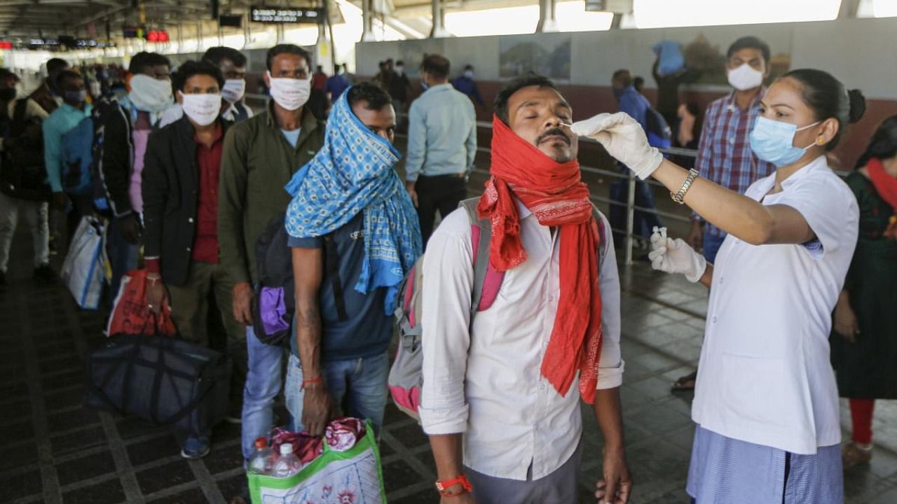  health worker collects a swab sample of a passenger for the Covid-19 test, at Kalupur Railway station. Credit: PTI Photo