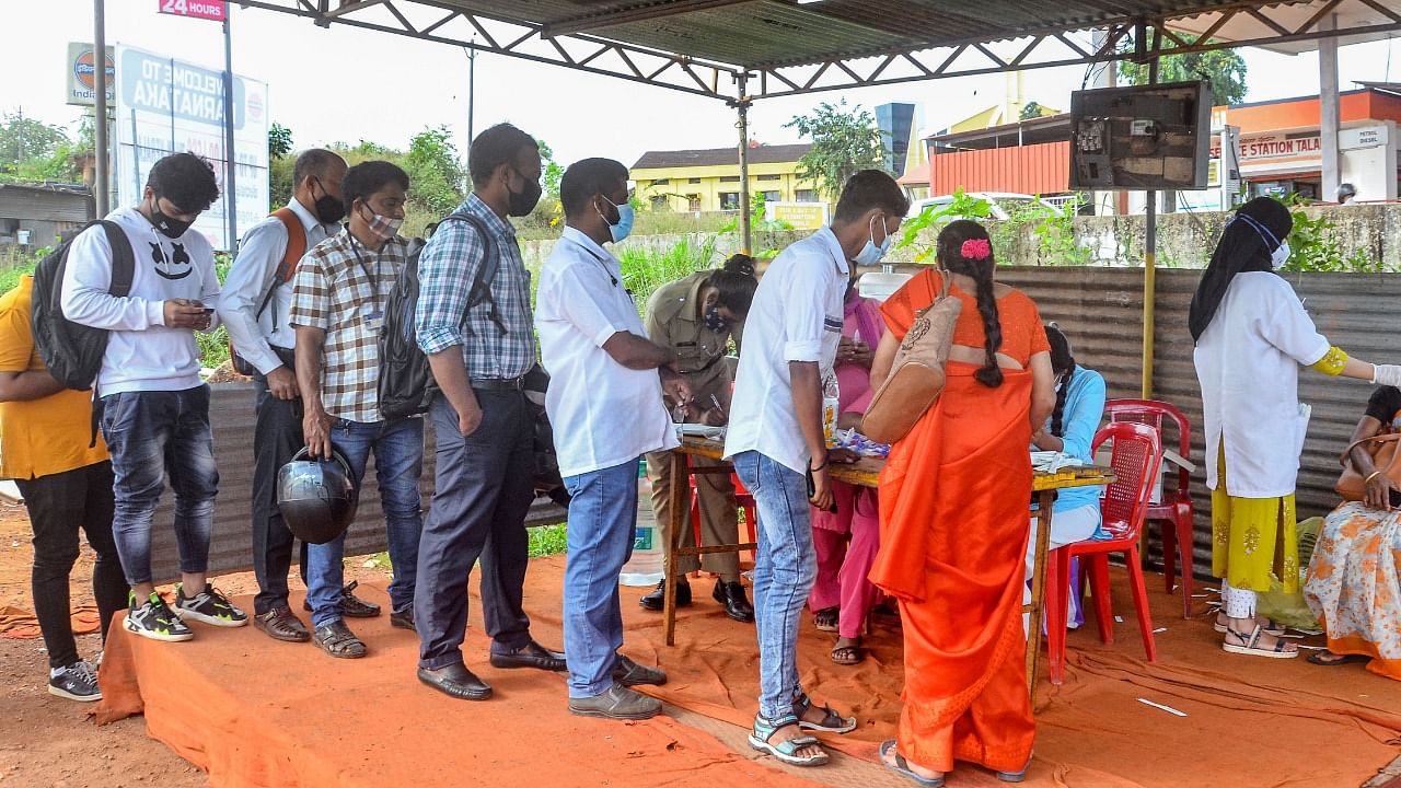 Commuters stand in a queue as others undergo RT-PCR COVID-19 testing at Talapady checkpost of the Karnataka-Kerala state border. Credit: DH Photo