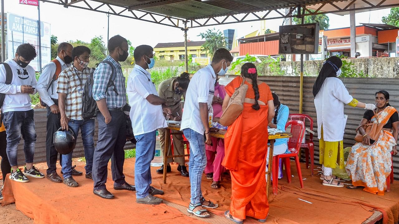 Commuters stand in a queue as others undergo RT-PCR Covid-19 testing at Talapady checkpost of the Karnataka-Kerala state border, in Mangaluru. Credit: PTI Photo