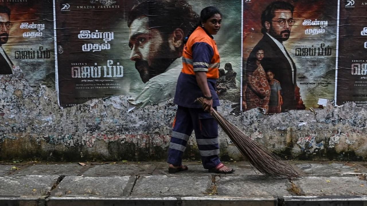 Sanitation worker walks past a poster of actor Suriya Sivakumar from the movie Jai Bhim in Chennai. Credit: AFP Photo