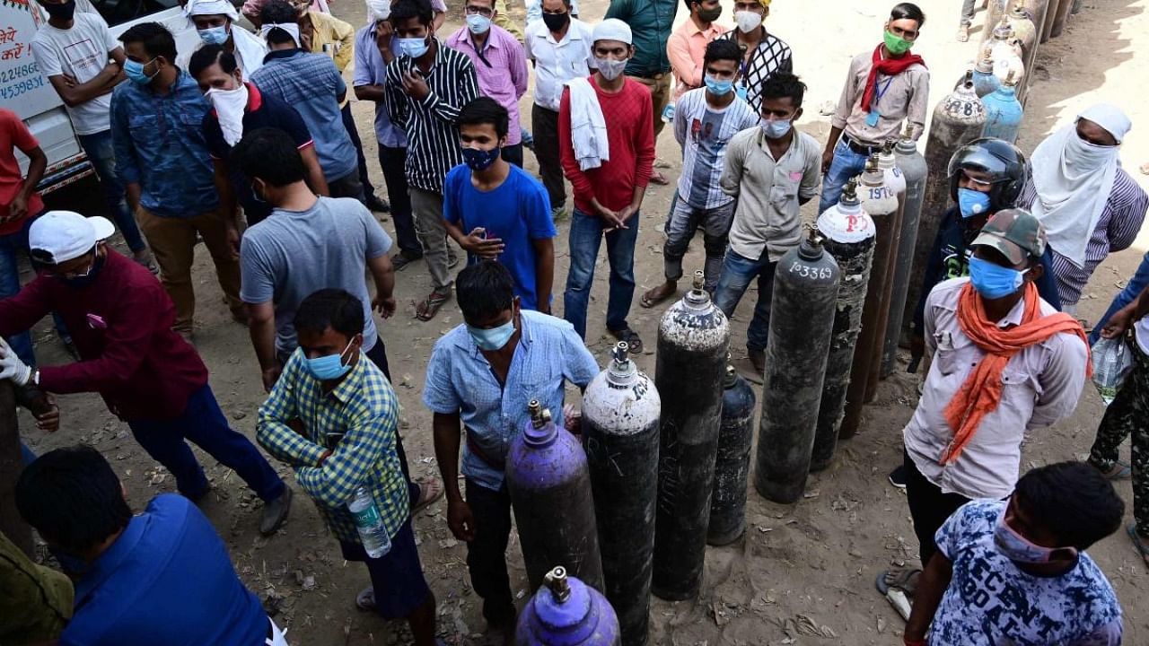 Family members stand in the queue to refill medical oxygen cylinders for COVID-19 patients at the oxygen refilling station, in Prayagraj. Credit: PTI Photo