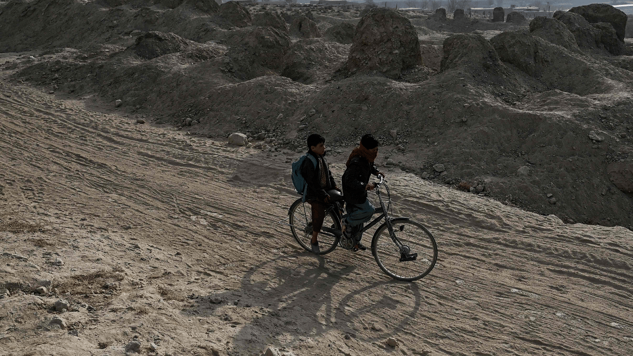 Children ride a bicycle along a path next to the ruins of destroyed houses in Arzo village on the outskirts of Ghazni. Credit: AFP Photo