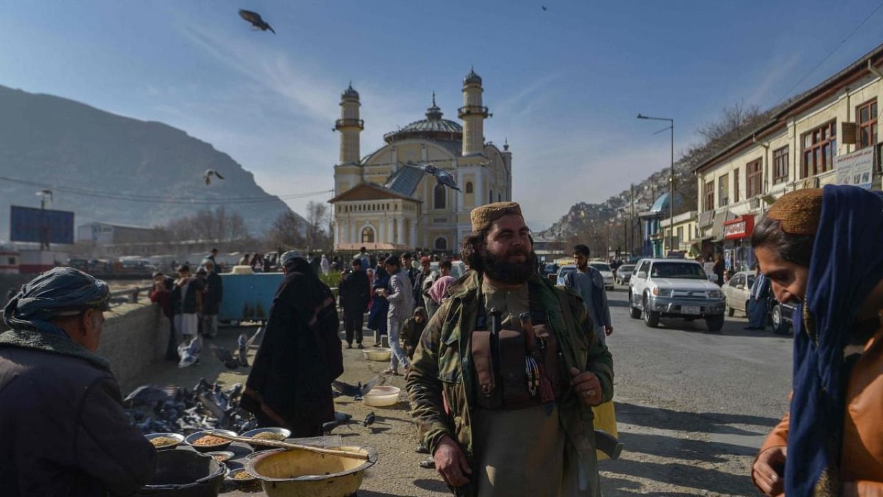 A member of the Taliban stands next to an Afghan hawker selling bird feed at a market area in Kabul. Credit: AFP Photo
