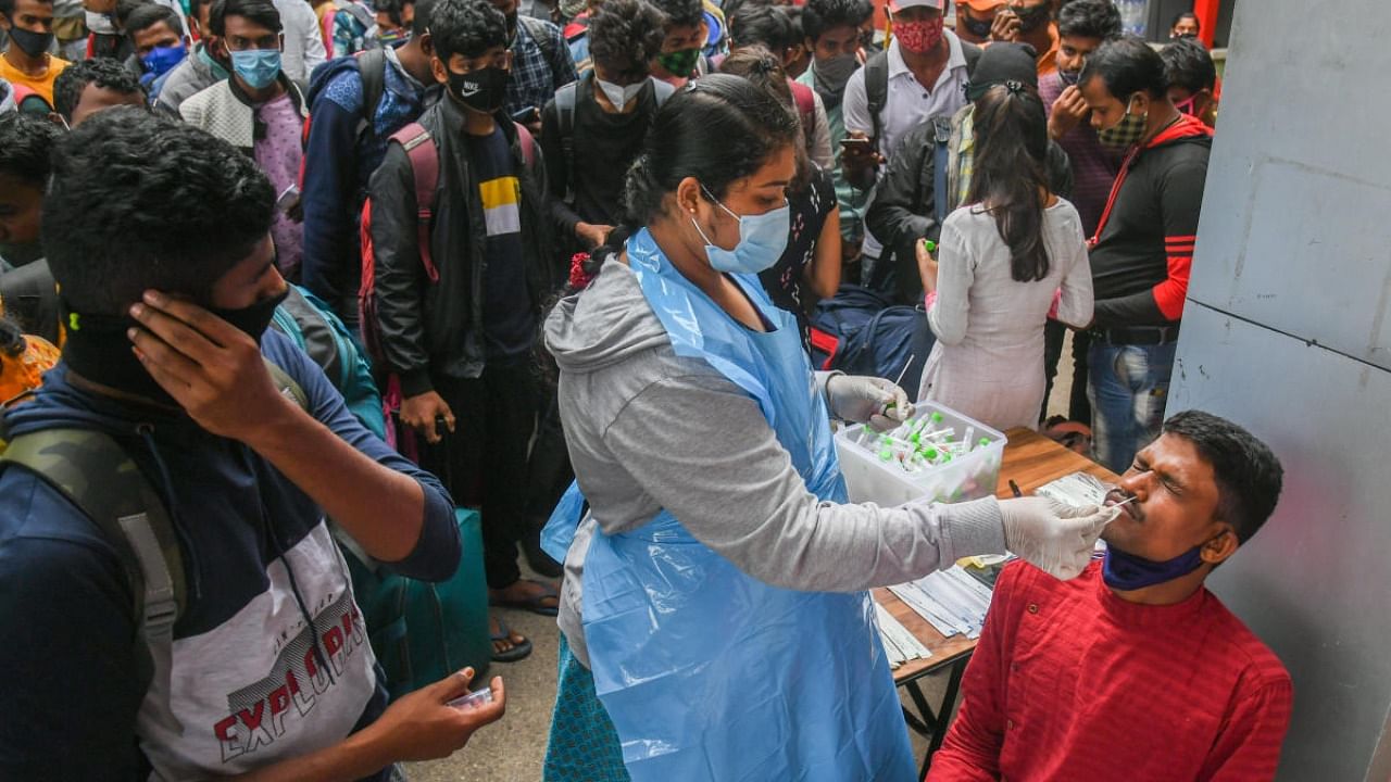 A health worker collects swab for Covid test from a passenger at KSR Railway Station in Bengaluru on Friday. Credit: DH Photo